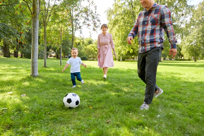 Szczęśliwa matka, ojciec i mały syn z piłką grający w piłkę w letnim parku