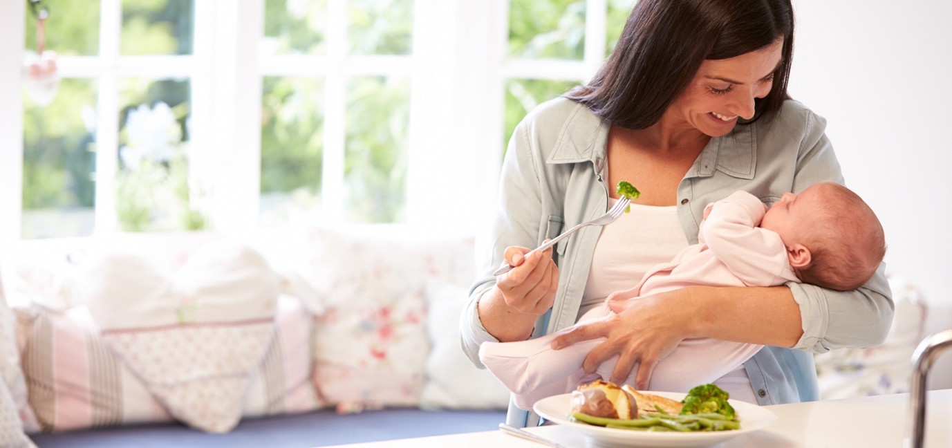 Breastfeeding mom holding newborn baby while having a meal
