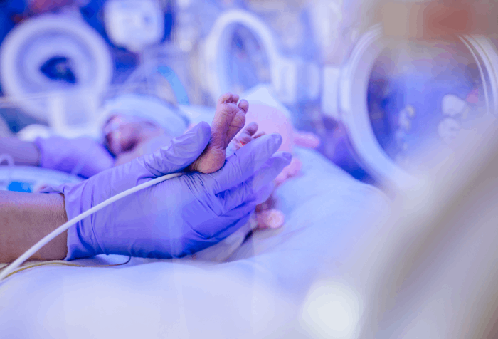 Dziecko w inkubatorze i badające je dłonie lekarza