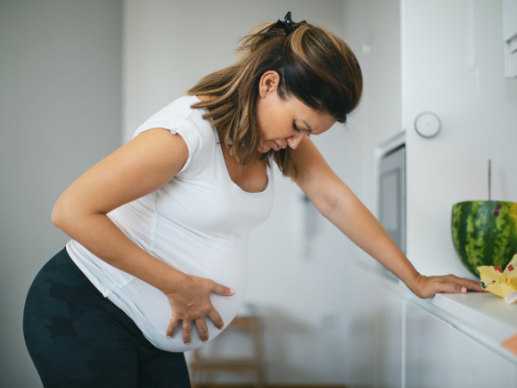 Kobieta w ciąży stoi w kuchni i odczuwa skurcze
