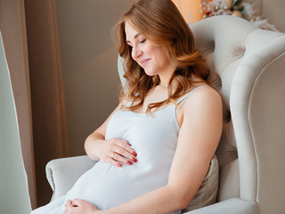 Kobieta w III trymestrze ciąży siedzi w fotelu i trzyma się za brzuch
