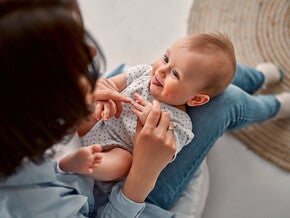 Photograph: smiling baby on caregiver's lap, reaching for hands in cozy room