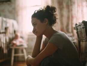 Wyczerpana mama siedząca przy łóżeczku dziecka, która być może cierpi na wypalenie rodzicielskie TITLE: Wypalenie rodzicielskie – wyczerpana mama siedząca przy łóżeczku dziecka | Nestlé FamilyNes