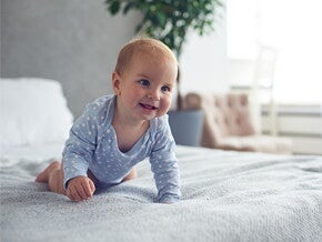8-miesięczny szczęśliwy chłopiec czołgający się na łóżku w domu