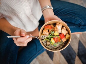 Zdrowa dieta po CC – kobieta oparta o blat i trzymająca talerz ze zdrowym śniadaniem