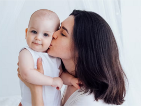 Młoda mama trzymająca dziecko i całująca je w policzek