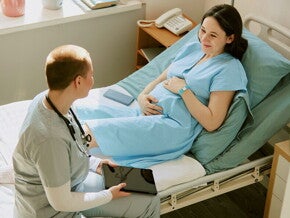 Położna siedząca na łóżku obok uśmiechniętej kobiety w ciąży