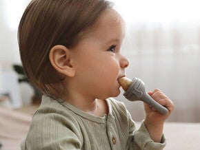 Toddler in green shirt holding a toy hammer indoors.