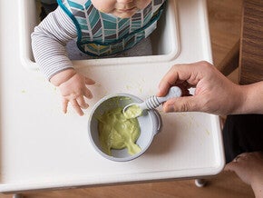 Baby in high chair eats avocado puree.