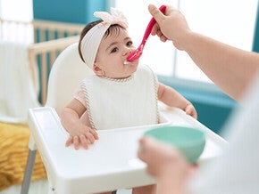 Baby in highchair being fed with a spoon.