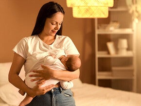 Woman breastfeeding a baby in a softly lit bedroom.