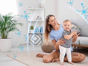 Woman in a living room helping a toddler learn to walk.