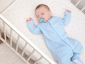 Baby in blue sleepsuit lying in a crib.