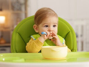 Toddler in a highchair with a yellow bowl on the tray.