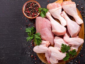 Raw chicken drumsticks with herbs and peppercorns on wooden board