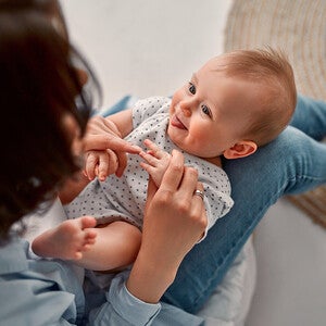 Photograph: smiling baby on caregiver's lap, reaching for hands in cozy room