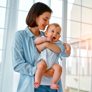 Uśmiechnięta mama trzyma na rękach kilkumiesięczne niemowlę | Nestlé FamilyNes Jak zatrzymać laktację: mama trzymająca na rękach kilkumiesięczne niemowlę
