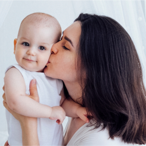 Młoda mama trzymająca dziecko i całująca je w policzek Młoda mama trzymająca dziecko i całująca je w policzek