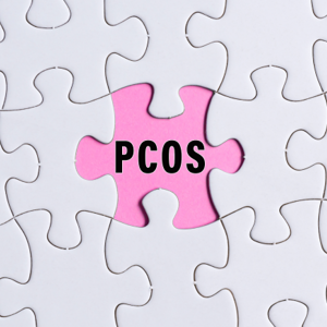 Zespół policystycznych jajników: czarny napis PCOS na różowym tle obok białych puzzli 