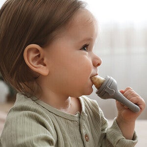 Toddler in green shirt holding a toy hammer indoors.