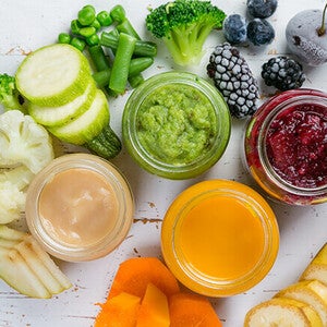 Jars of colorful purees surrounded by fresh fruits and vegetables on a rustic surface.