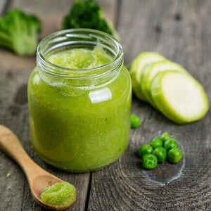 Green vegetable puree in a jar with zucchini and peas on a wooden table.