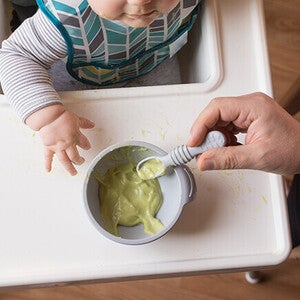 Baby in high chair eats avocado puree.