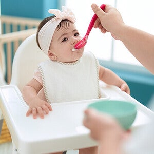 Baby in highchair being fed with a spoon.