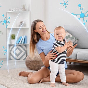Woman in a living room helping a toddler learn to walk.