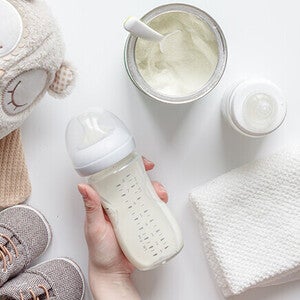 Baby essentials: bottle, formula, plush toy, shoes, and cloth on white background.