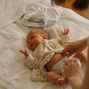 Baby on bed getting diaper changed, wearing striped outfit.