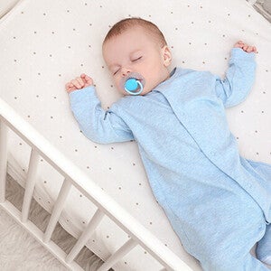 Baby in blue sleepsuit lying in a crib.