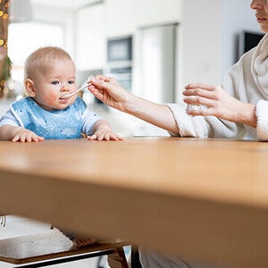 Feeding baby at kitchen table, morning light.