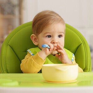 Toddler in a highchair with a yellow bowl on the tray.