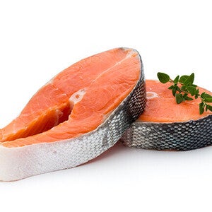Two raw salmon steaks with herbs on top.