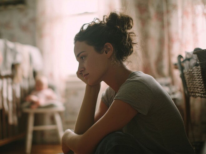 Wyczerpana mama siedząca przy łóżeczku dziecka, która być może cierpi na wypalenie rodzicielskie TITLE: Wypalenie rodzicielskie – wyczerpana mama siedząca przy łóżeczku dziecka | Nestlé FamilyNes