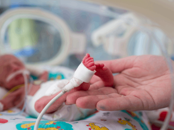 Dziecko w inkubatorze, jego stopa spoczywa w dłoni rodzica