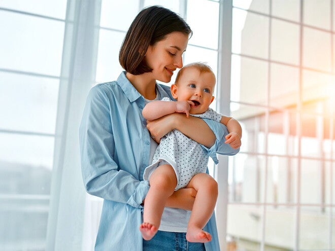 Uśmiechnięta mama trzyma na rękach kilkumiesięczne niemowlę | Nestlé FamilyNes Jak zatrzymać laktację: mama trzymająca na rękach kilkumiesięczne niemowlę
