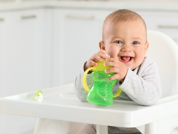Maluszek siedzi w krzesełku, w ręce trzyma bidon z elektrolitami dla niemowląt