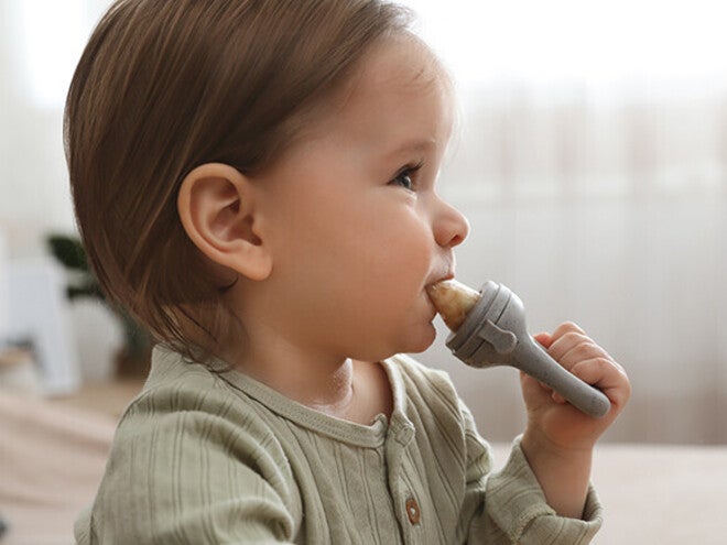 Toddler in green shirt holding a toy hammer indoors.