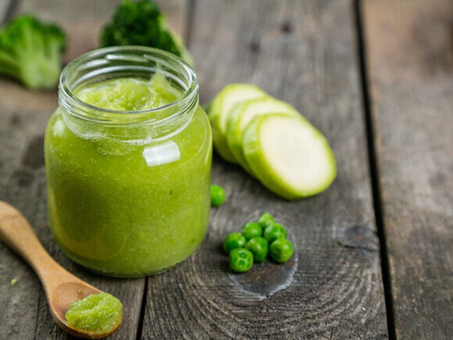 Green vegetable puree in a jar with zucchini and peas on a wooden table.