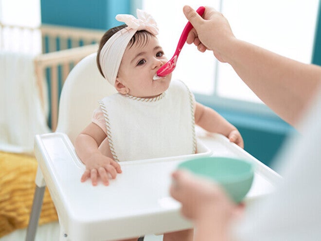 Feeding a baby in a high chair with a spoon.