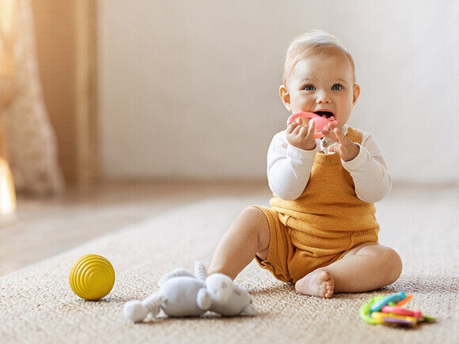Baby in yellow overalls sitting on floor with toys nearby.
