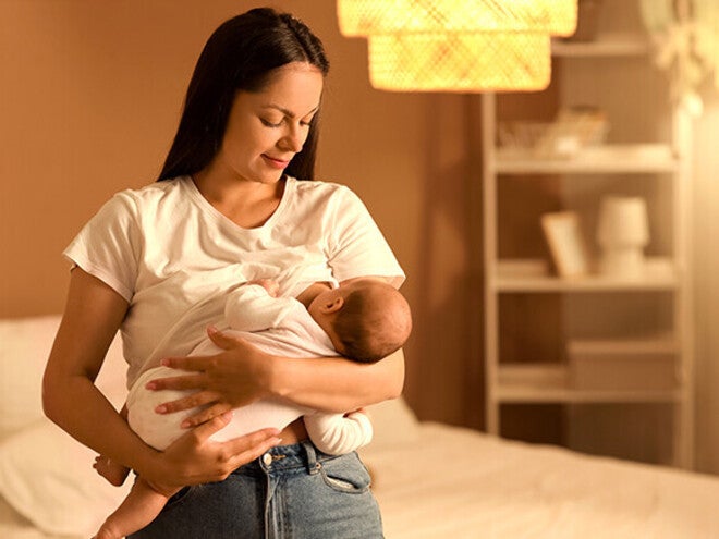 Woman breastfeeding a baby in a softly lit bedroom.