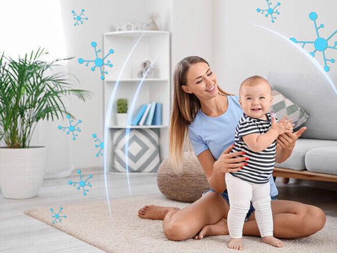 Woman in a living room helping a toddler learn to walk.