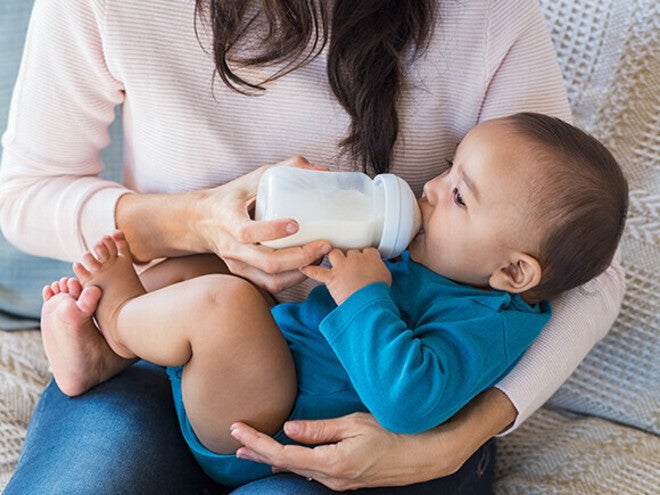 Person bottle-feeding a baby in blue clothes.