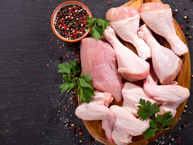 Raw chicken drumsticks with herbs and peppercorns on wooden board