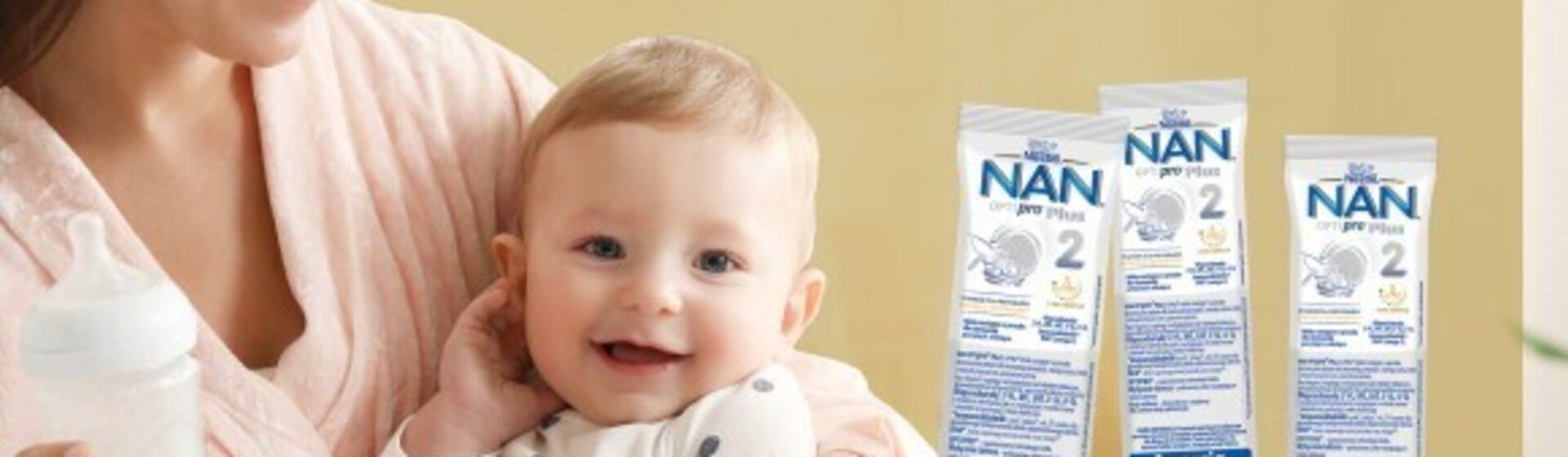 Uśmiechnięta kobieta trzyma dziecko; obok nich leżą produkty do pielęgnacji skóry.