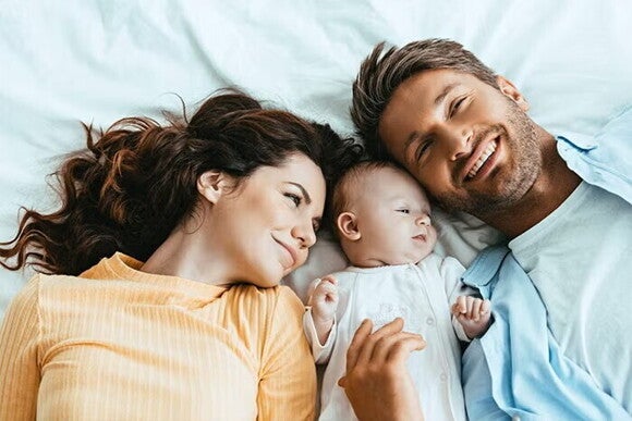 uśmiechnięci rodzice leżą na łóżku z dzieckiem uśmiechnięci rodzice leżą na łóżku z dzieckiem