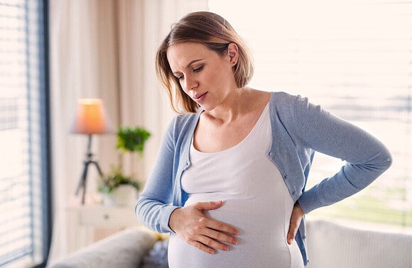 Kobieta w ciąży trzymająca się za brzuch i plecy z powodu dolegliwości trawiennych
